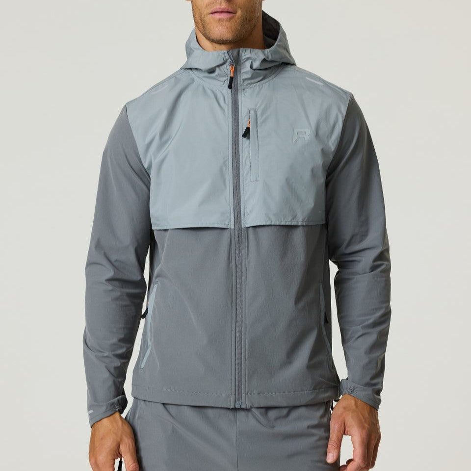 Man wearing a slate and light grey Reprimo Summit Windbreaker with hood and full zipper, designed for lightweight comfort and active movement