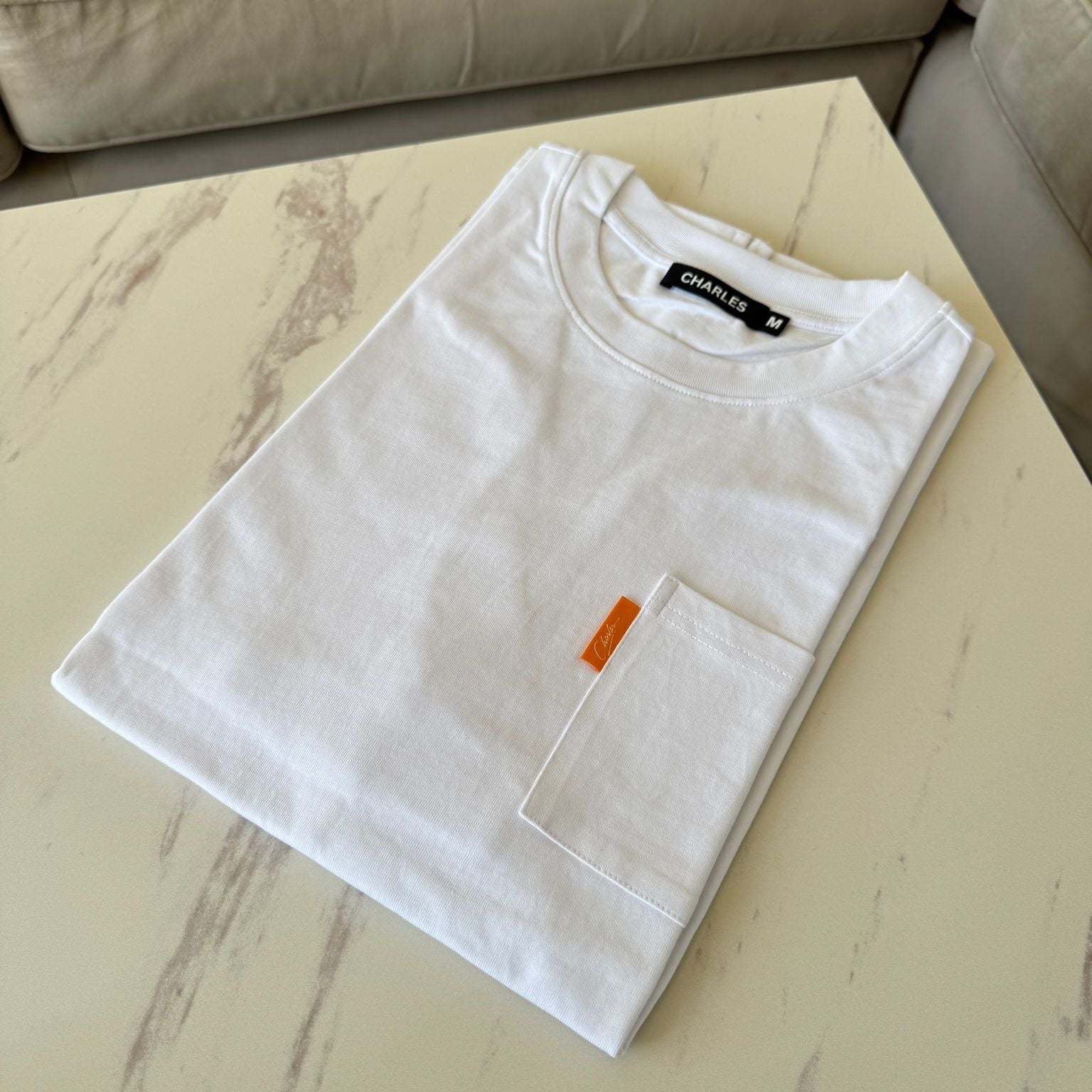 White Studio By Charles White pocket tee neatly folded on a marble table