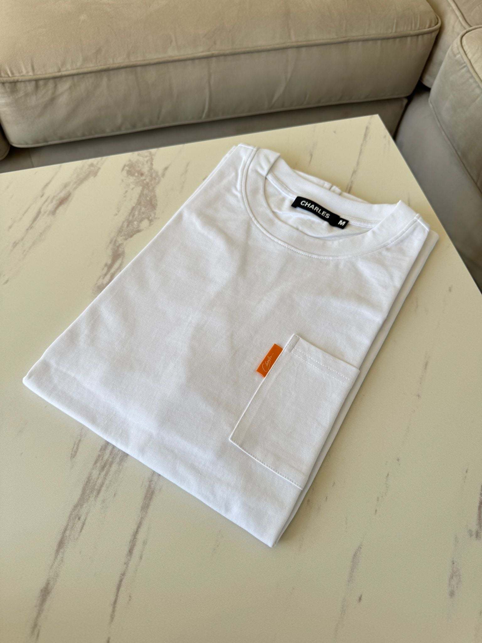 White Studio By Charles White pocket tee neatly folded on a marble table