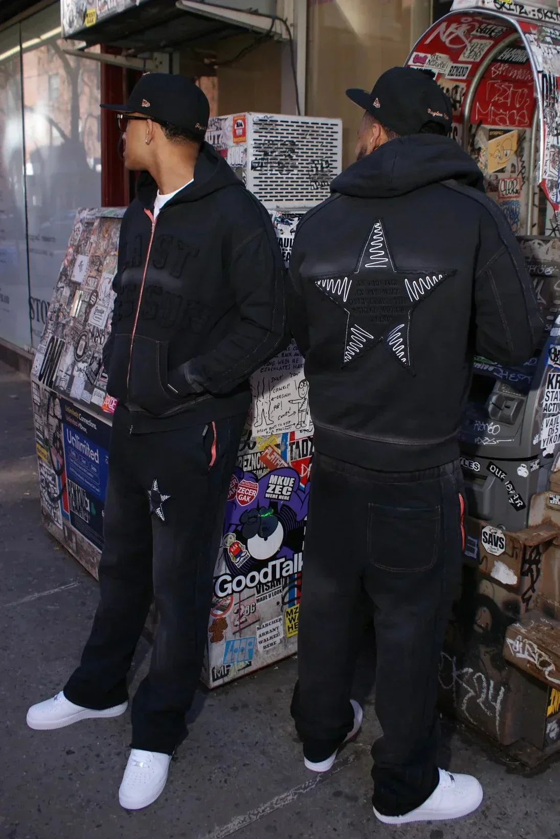 Black hoodie with star appliqué design on back, modeled by two people in an urban setting, Last Lesson Hoodie.