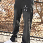 Black joggers with star appliqué and embroidered artwork, featuring a casual fit.