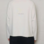 Back view of Natural Art Studio white appliqué long sleeve cotton shirt with screen print logo and boxy fit