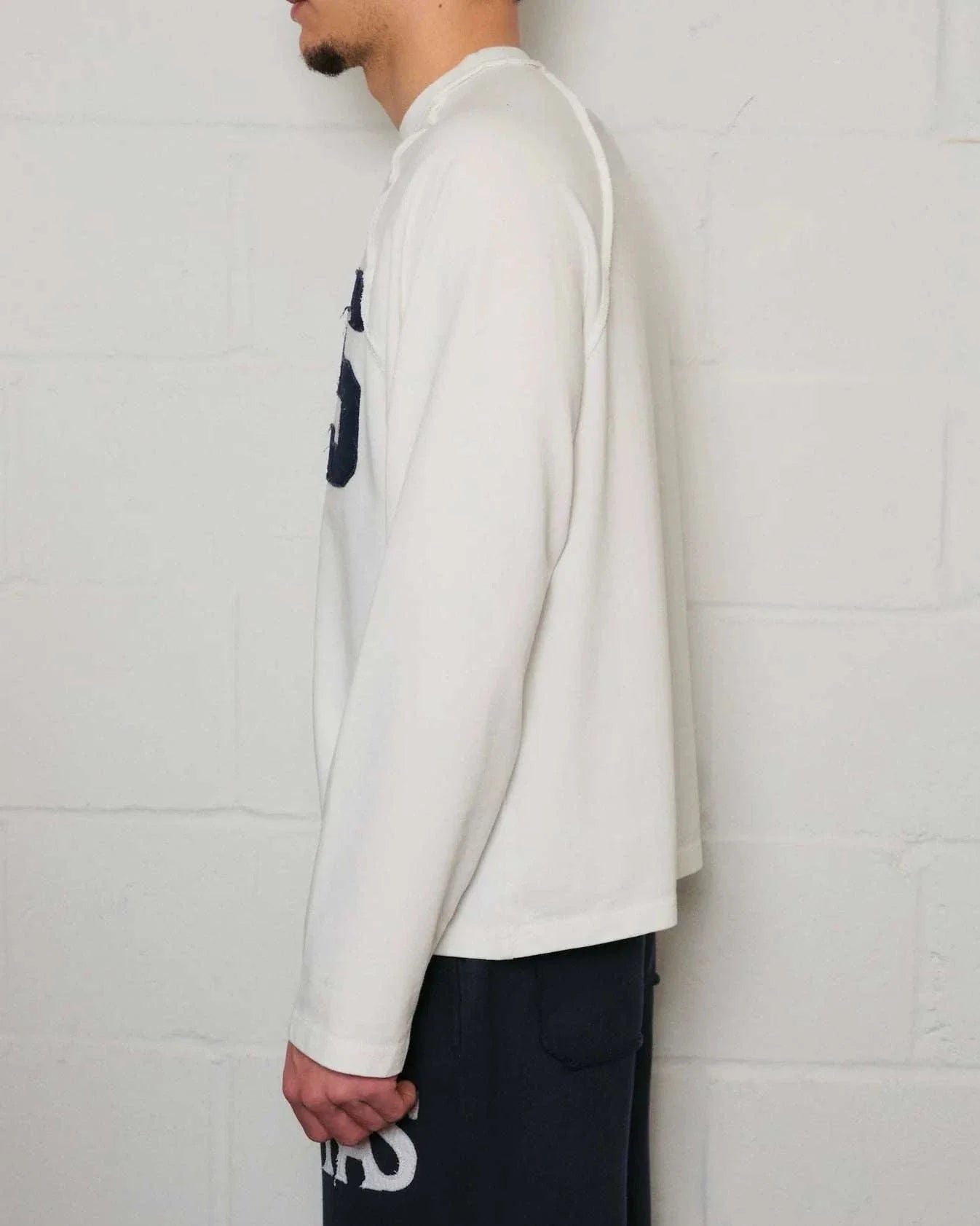Side view of a man wearing Natural Art Studio white long sleeve appliqué cotton shirt with boxy fit and dropped shoulders