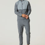 Man wearing Reprimo Summit Windbreaker in slate and light grey with matching pants and sneakers