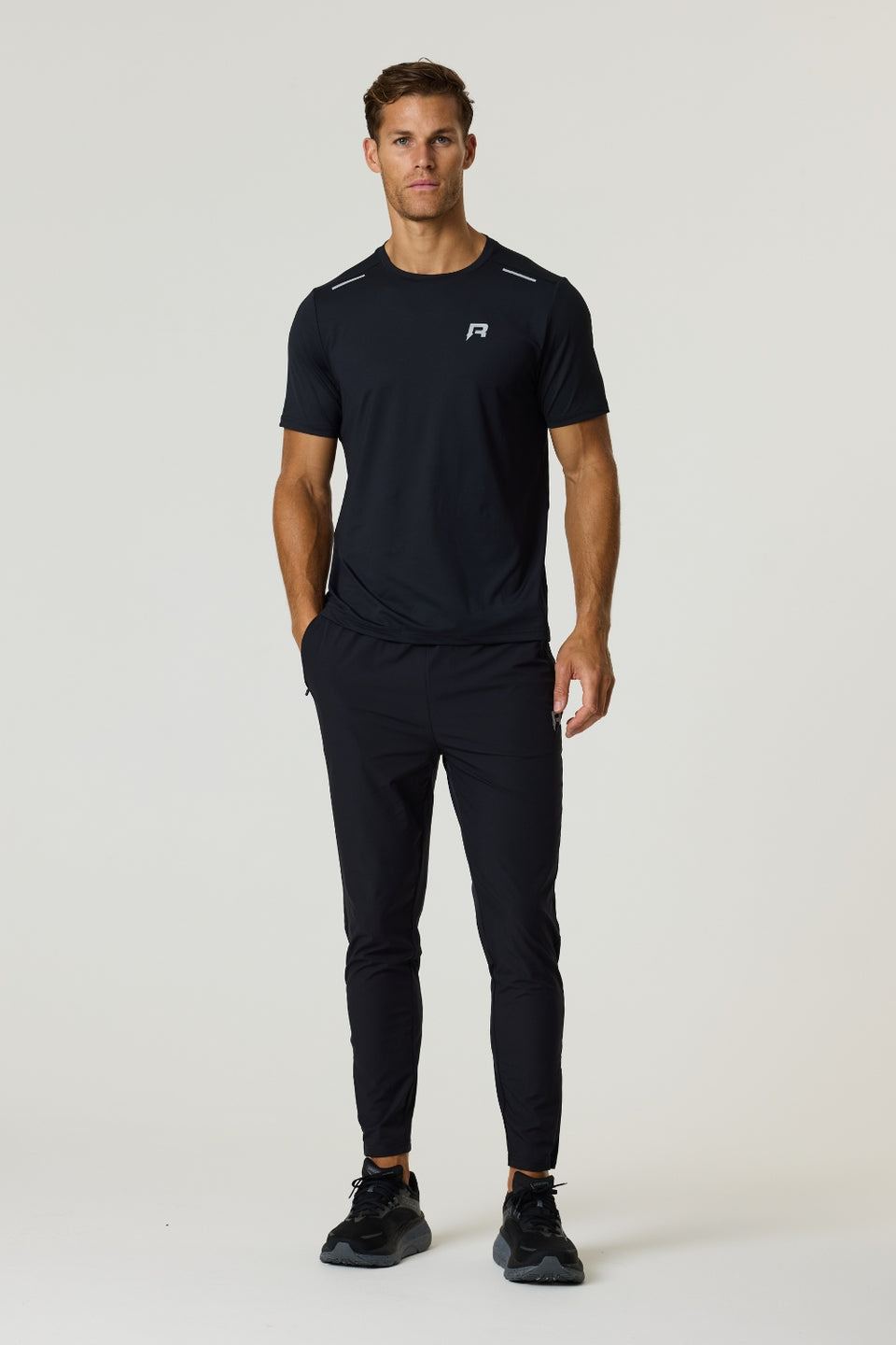 Male model wearing black Reprimo Flight T-Shirt and black athletic pants with black sneakers, standing against a plain light background.
