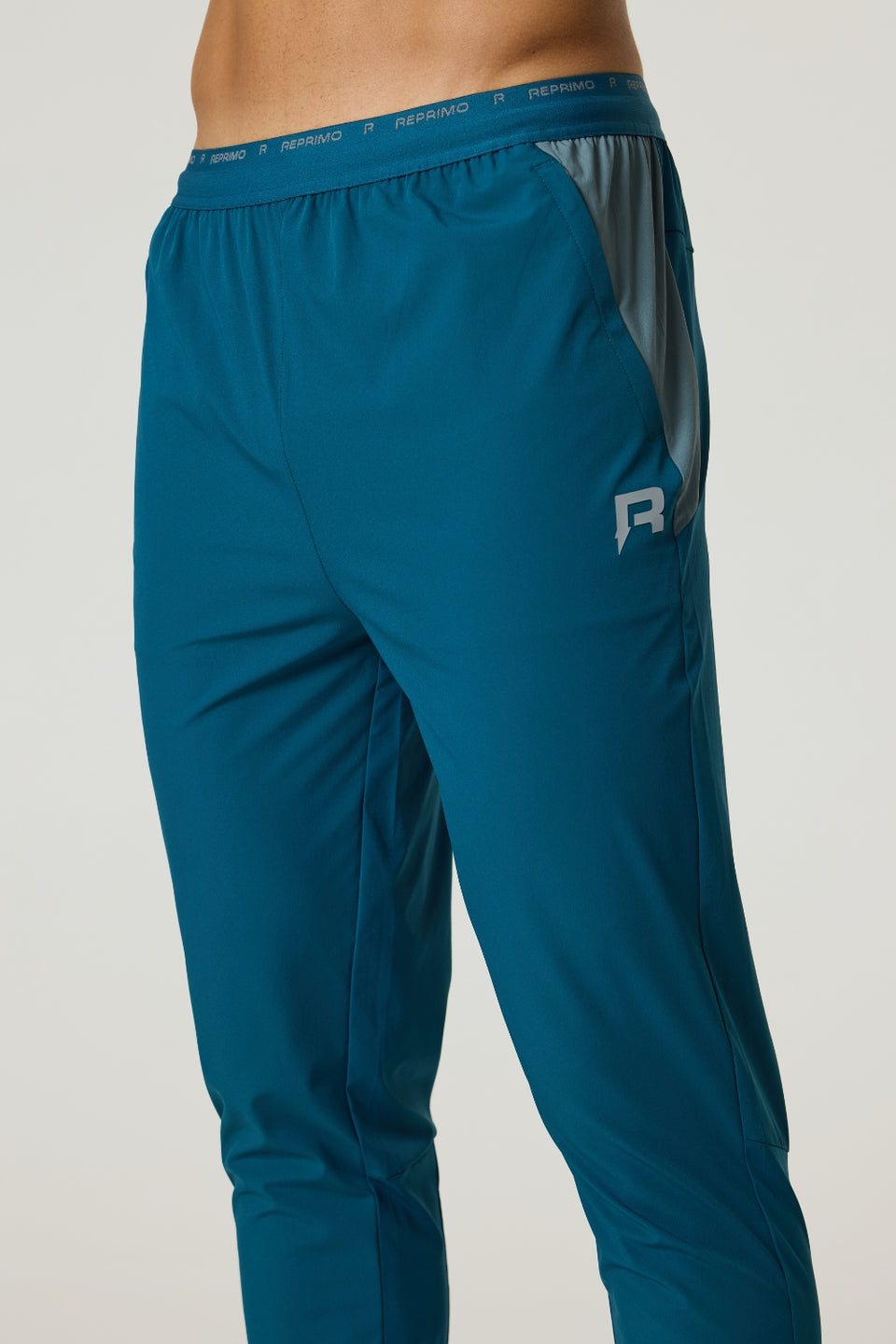 Men's Reprimo Flight Pants in tidal teal and blue steel with breathable fabric, reflective strips, and secure side pockets for active workouts.