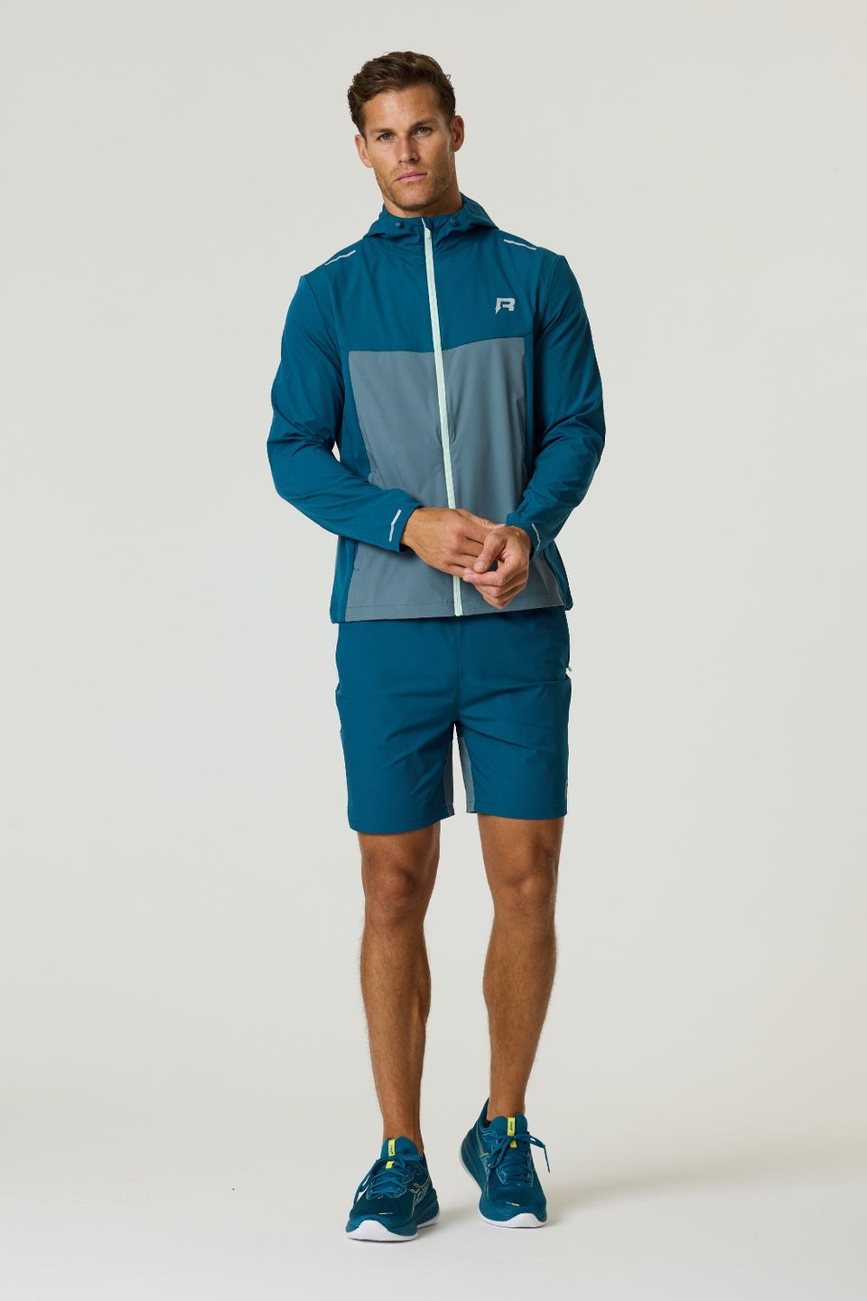 Man wearing Reprimo Flight Windbreaker in tidal teal and blue steel with matching shorts and running shoes