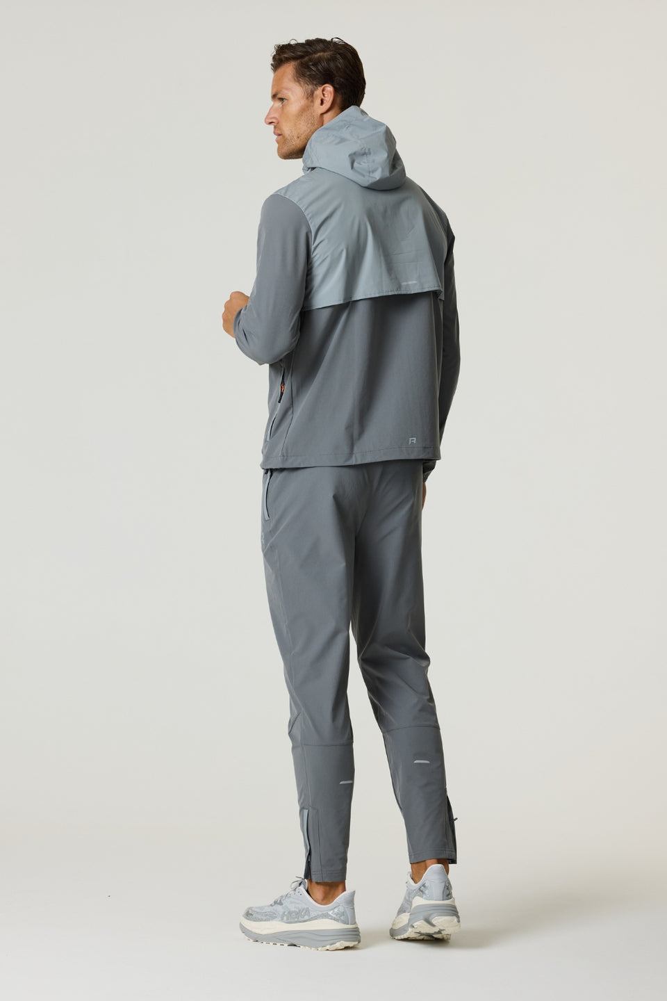 Man wearing slate and light grey Reprimo Summit Windbreaker with hood and matching pants, showcasing lightweight and reflective outdoor jacket.