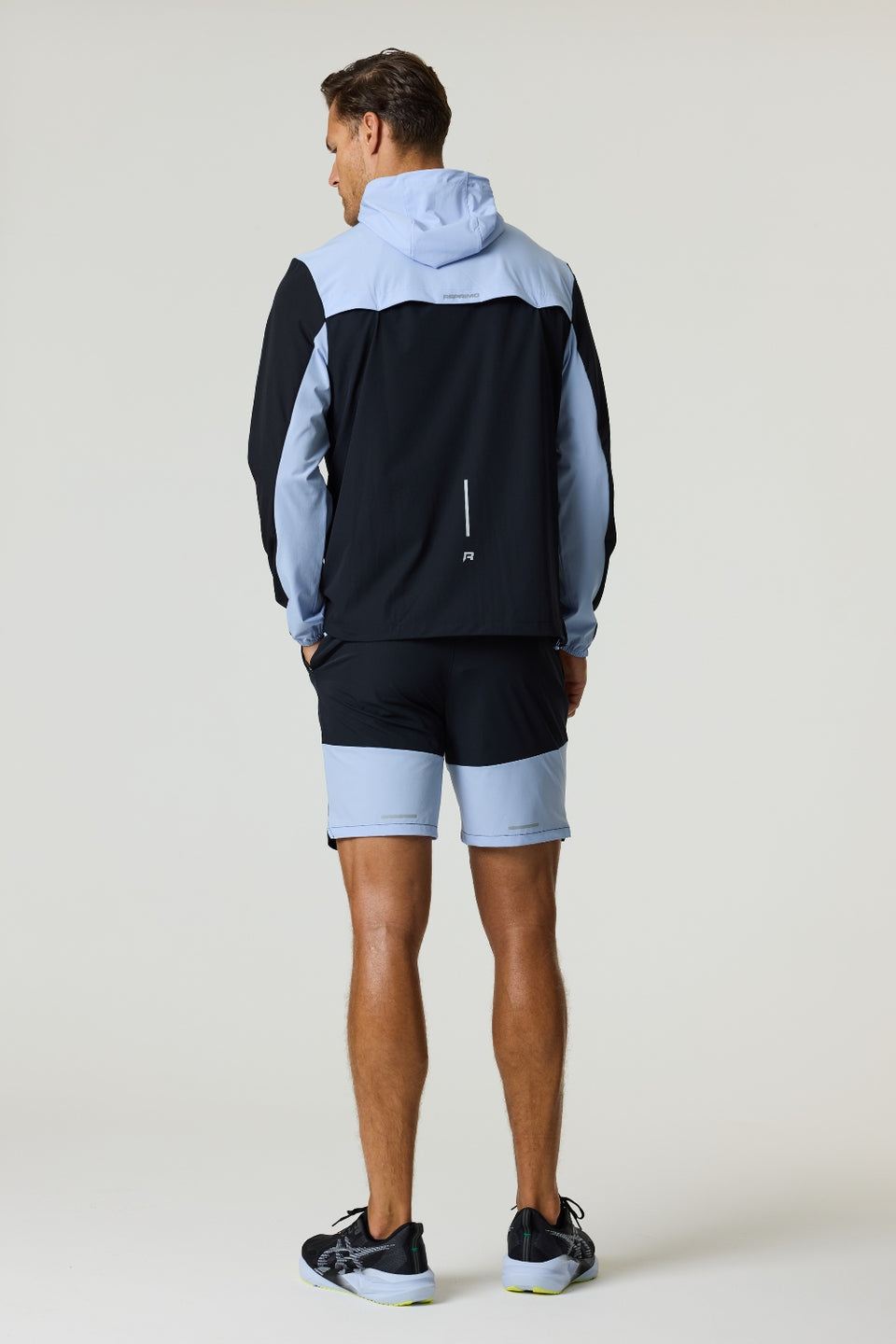 Man wearing black and dusky sky Reprimo Flight Windbreaker with hood and zip pockets, paired with matching shorts