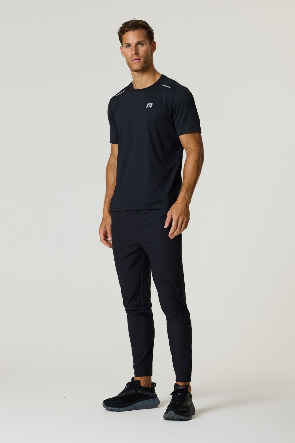 Male model wearing black Reprimo Flight Pants with reflective strips and functional pockets, paired with black athletic shirt and shoes.