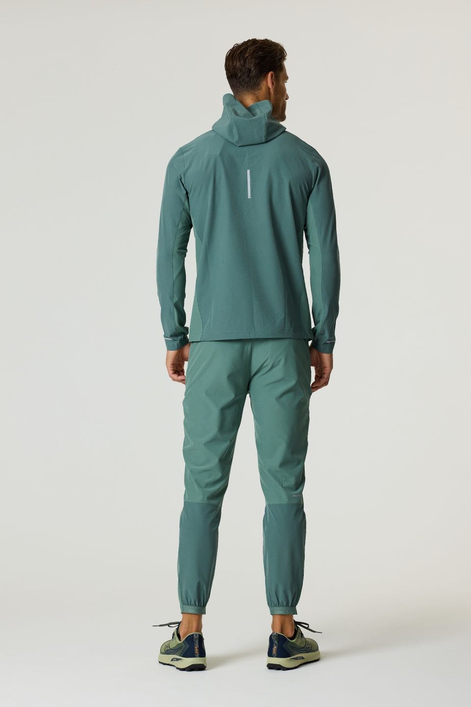 Man wearing botanical pine Reprimo Glide Jacket and matching pants standing back facing white background