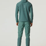 Man wearing botanical pine Reprimo Glide Jacket and matching pants standing back facing white background
