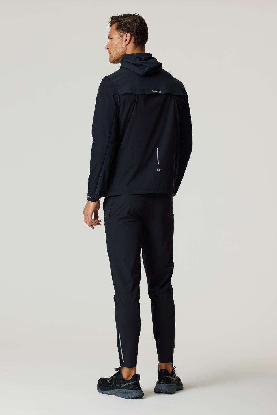 Rear view of man wearing black Reprimo Flight Windbreaker with hood and zip pockets, paired with black athletic pants and shoes.