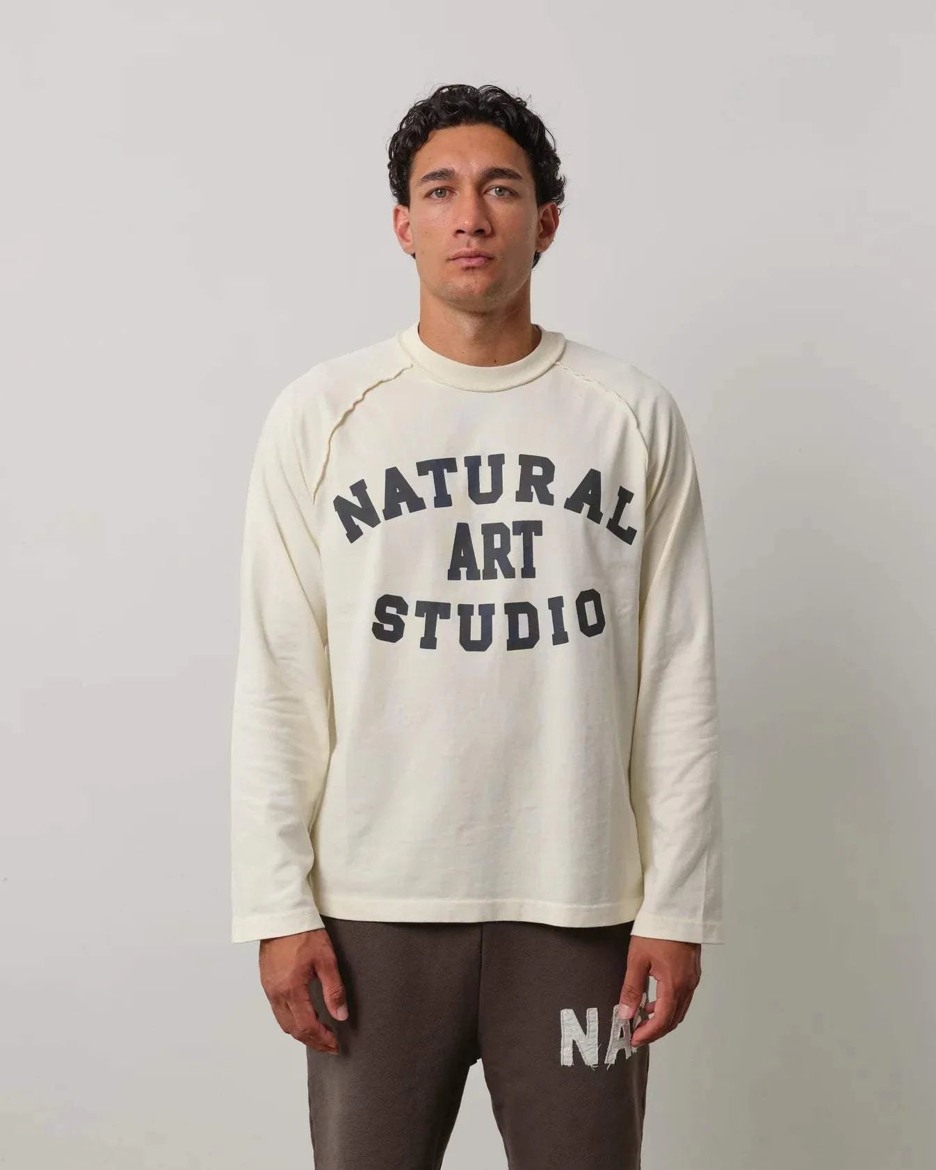 Man wearing Natural Art Studio Raglan long sleeve shirt with front logo print and raglan seams in cream color