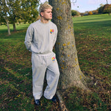 Man wearing grey Five Questions Rugby sweatshirt and matching pants outdoors by tree