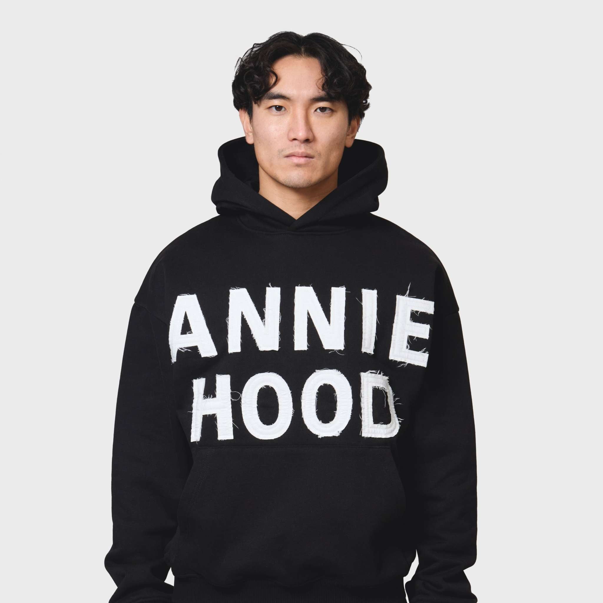 Black ANNIE HOOD APPLIQUE HOODY in relaxed fit on tall male model, 500gsm brushback cotton