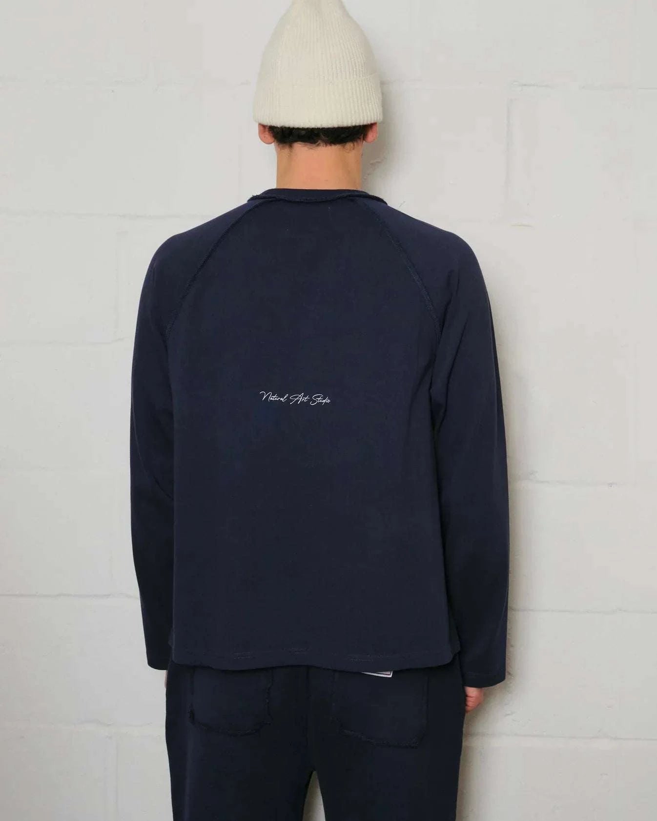Back view of Natural Art Studio navy raglan long sleeve shirt with inside out raglan seams and screen print logo, worn by model