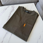 Folded khaki Studio By Charles pocket tee on white marble surface