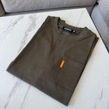 Folded khaki Studio By Charles pocket tee on white marble surface
