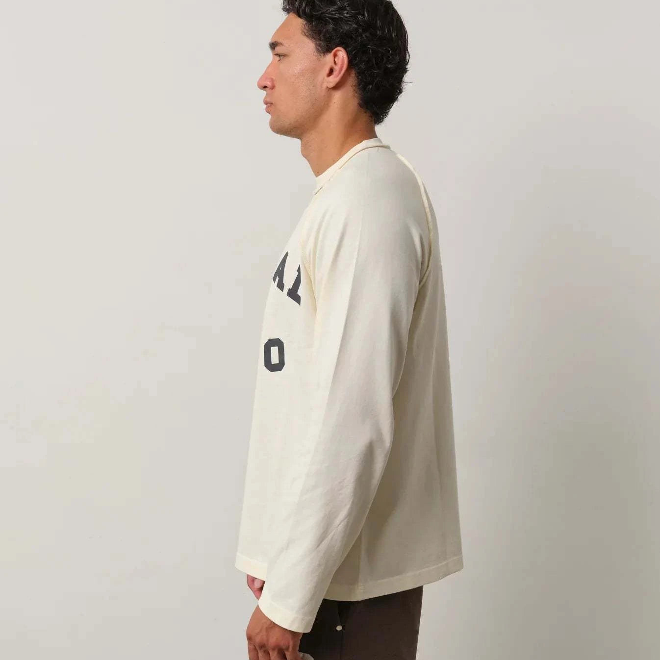 Man wearing Natural Art Studio Raglan long sleeve shirt in cream with boxy fit and printed logo