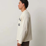 Man wearing Natural Art Studio Raglan long sleeve shirt in cream with boxy fit and printed logo