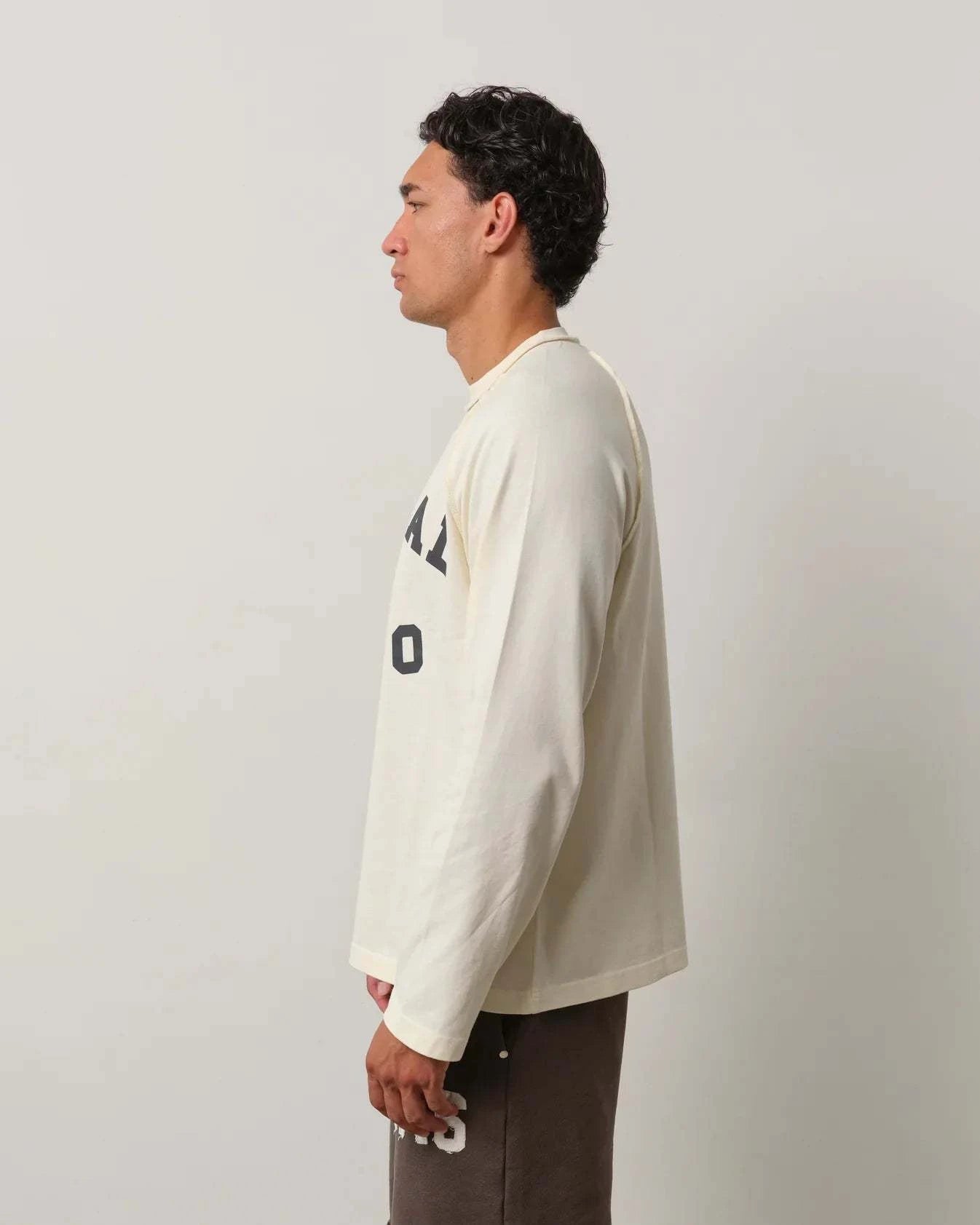 Man wearing Natural Art Studio Raglan long sleeve shirt in cream with boxy fit and printed logo
