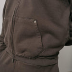 Close-up of brown Natural Art Studio NAS Appliqué Hoodie showing raw seams on cuffs and metal rivet on pocket detail