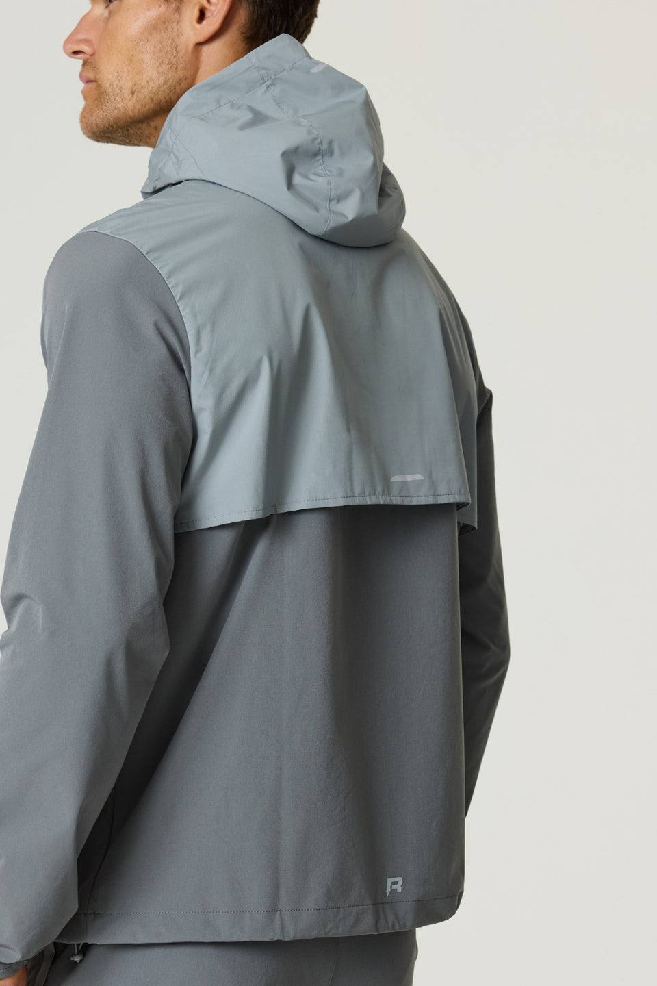 Man wearing Reprimo Summit Windbreaker in slate and light grey with hood and reflective details, shown from the back