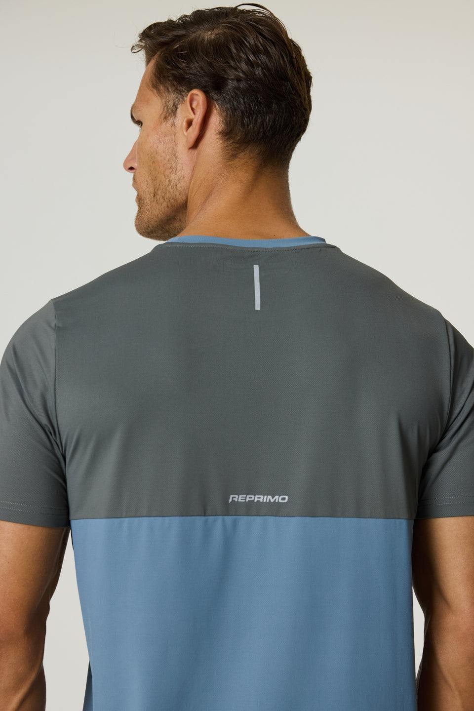 Back view of a man wearing a Reprimo Flight T-Shirt in Air Force Blue and Gunmetal with reflective strip and logo, showcasing athletic fit and lightweight breathable fabric