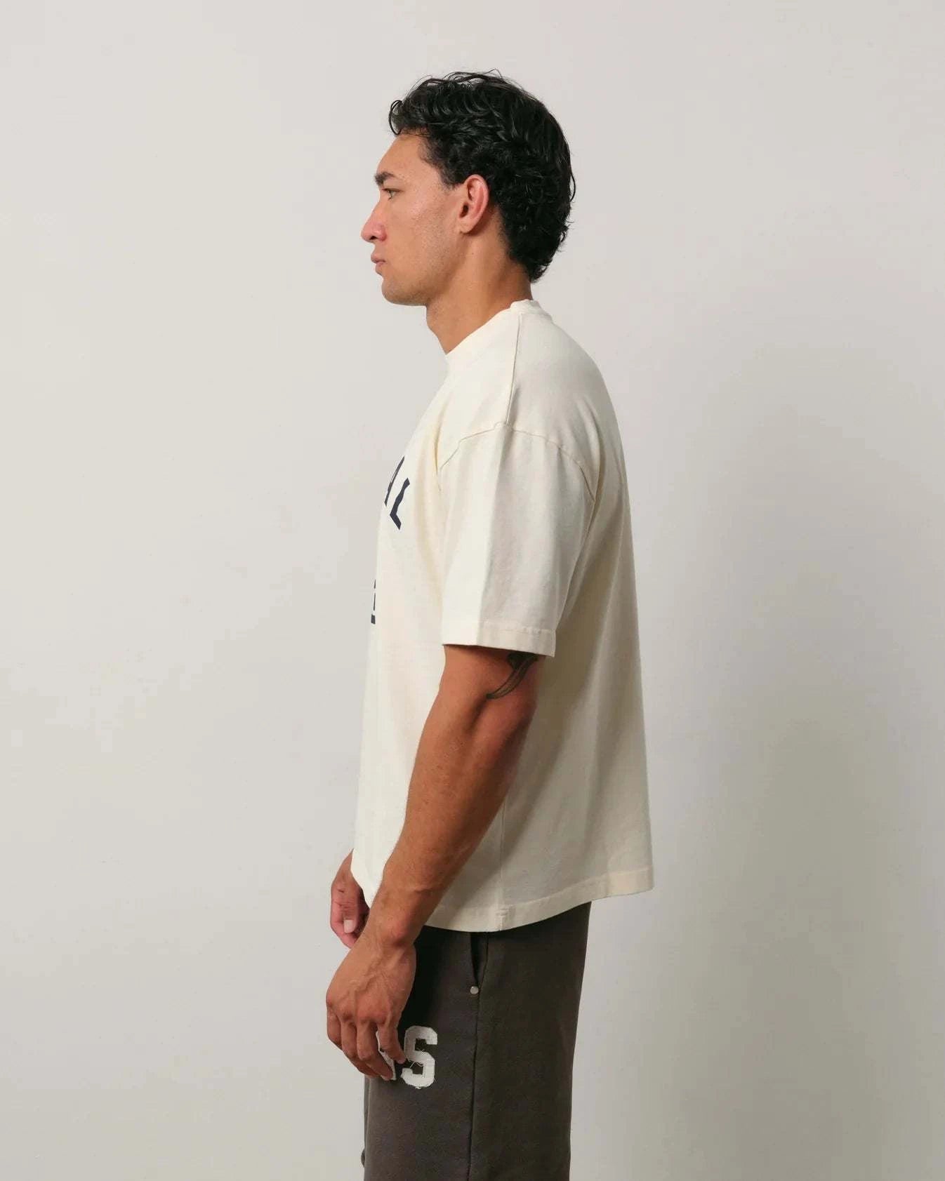 Natural Art Studio Varsity Tee 100% cotton boxy fit oversized drop shoulder cream shirt with front and back screen print logo worn by male model side view