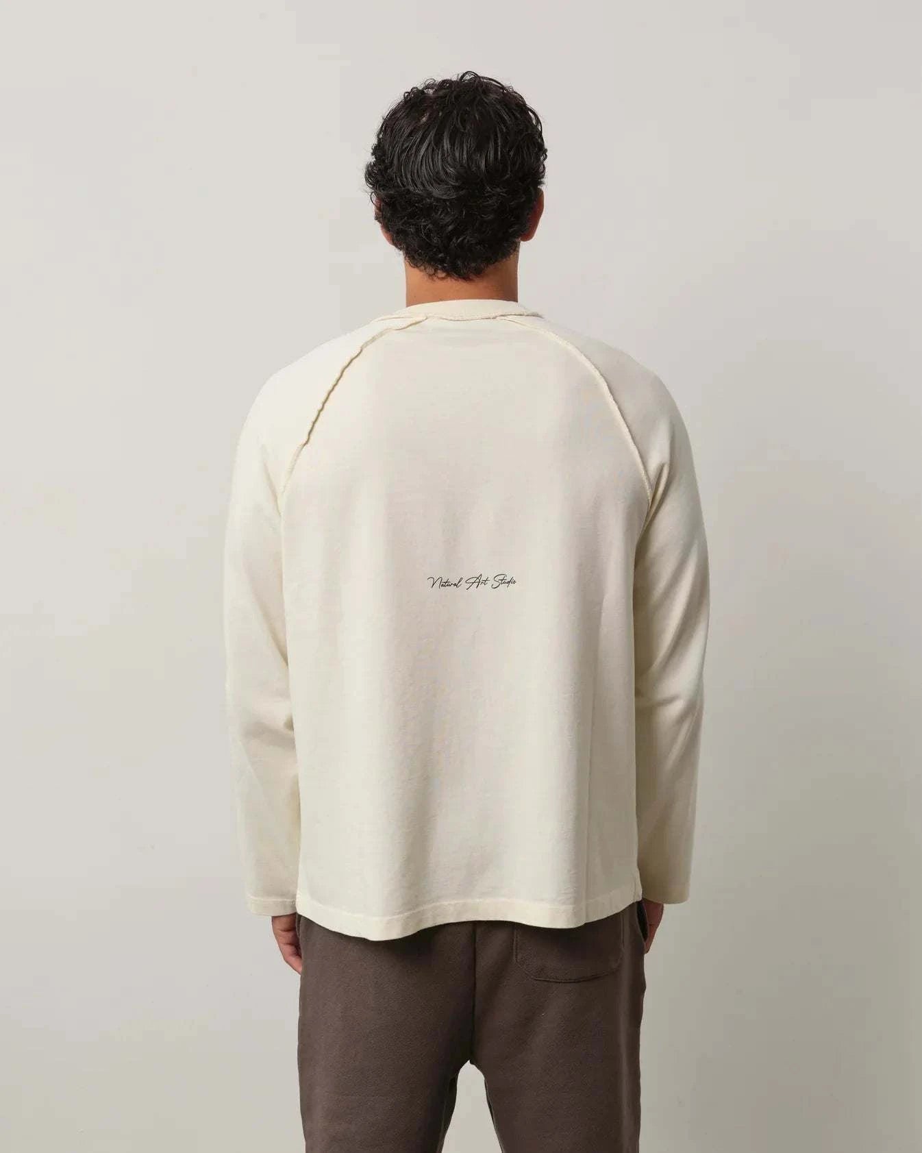 Man wearing Natural Art Studio Raglan long sleeve shirt with inside-out raglan seams and a boxy fit, shown from the back