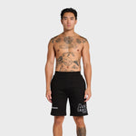 Male model wearing black ANNIE HOOD College Shorts with logo detailing against plain background