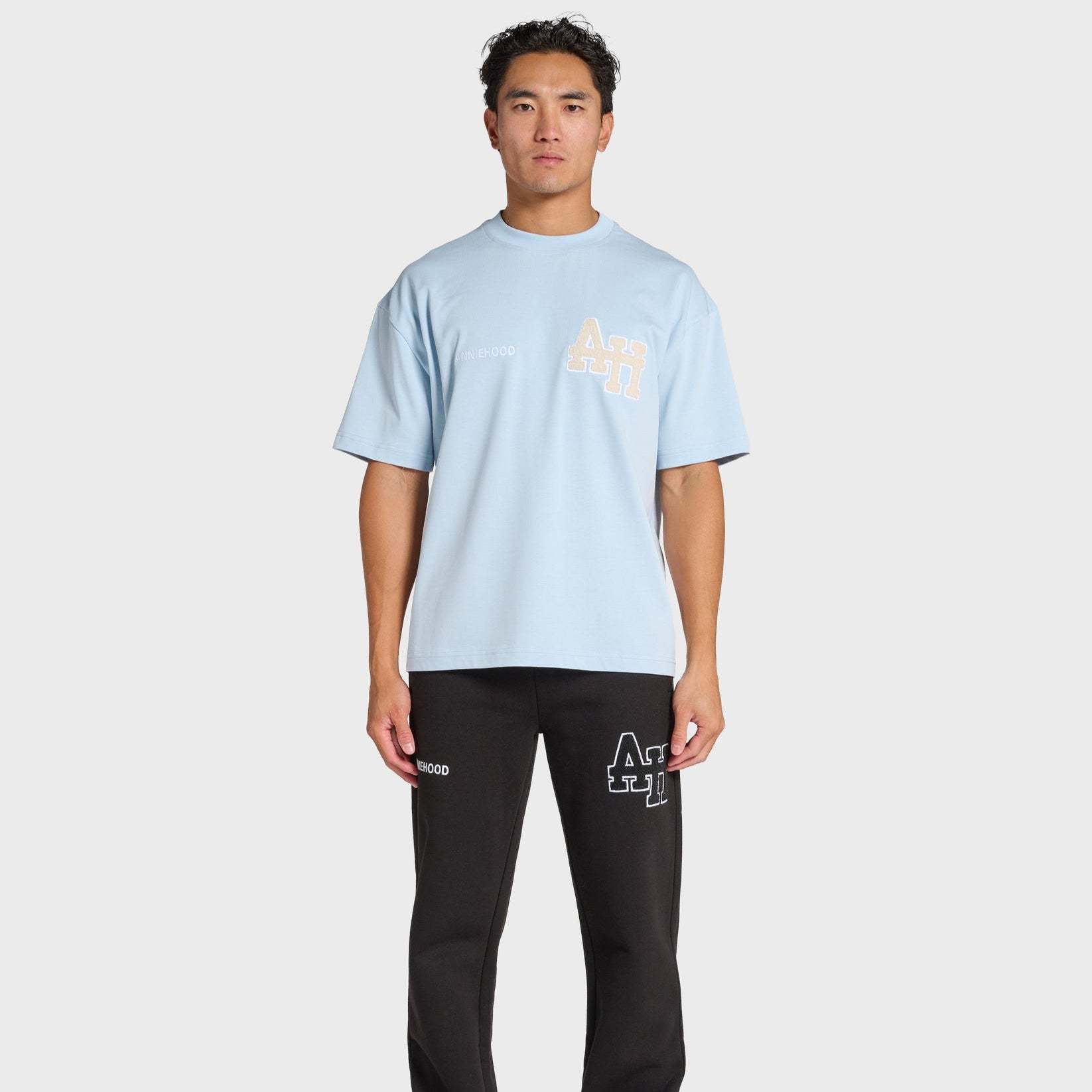 Man wearing baby blue ANNIE HOOD college t-shirt and black pants with logos