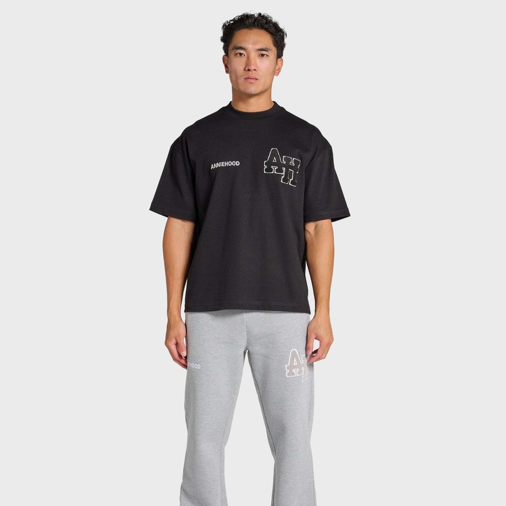 Man wearing black ANNIE HOOD College T-Shirt with gray sweatpants on white background