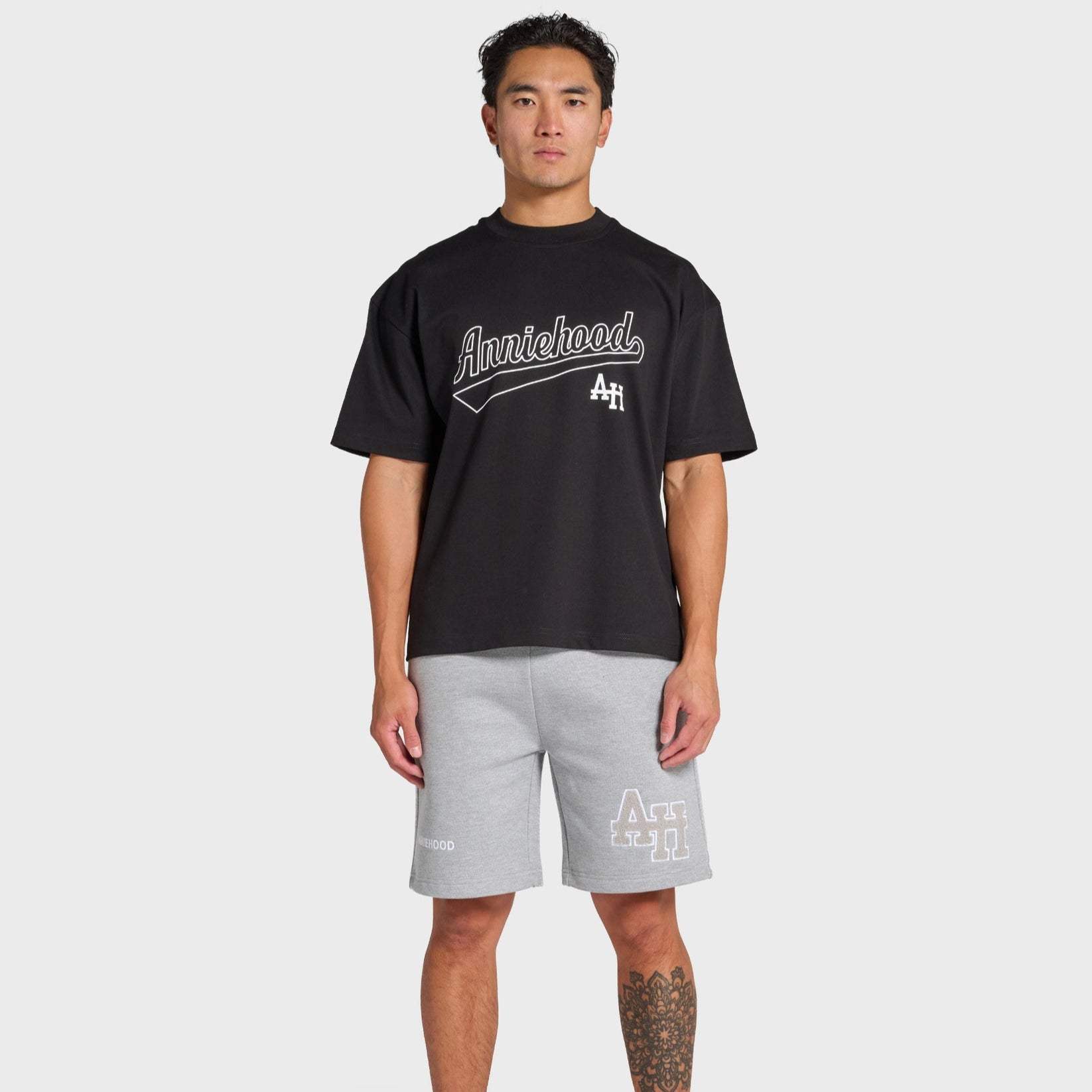 Man wearing black ANNIE HOOD Baseball T-shirt and gray shorts