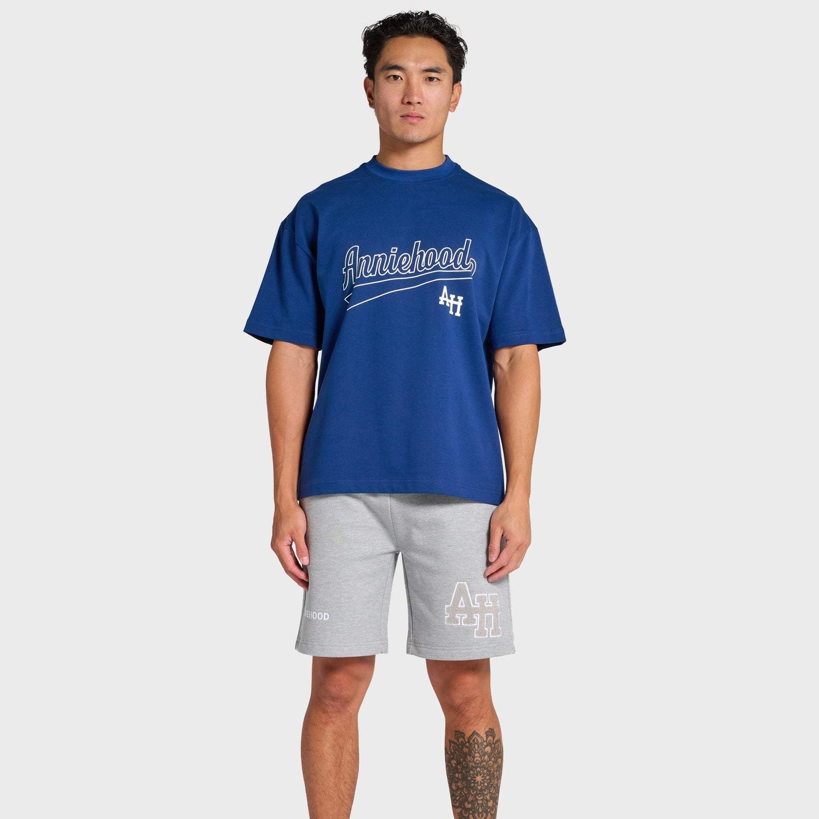 Male model wearing ANNIE HOOD navy blue baseball T-shirt with white logo and gray shorts