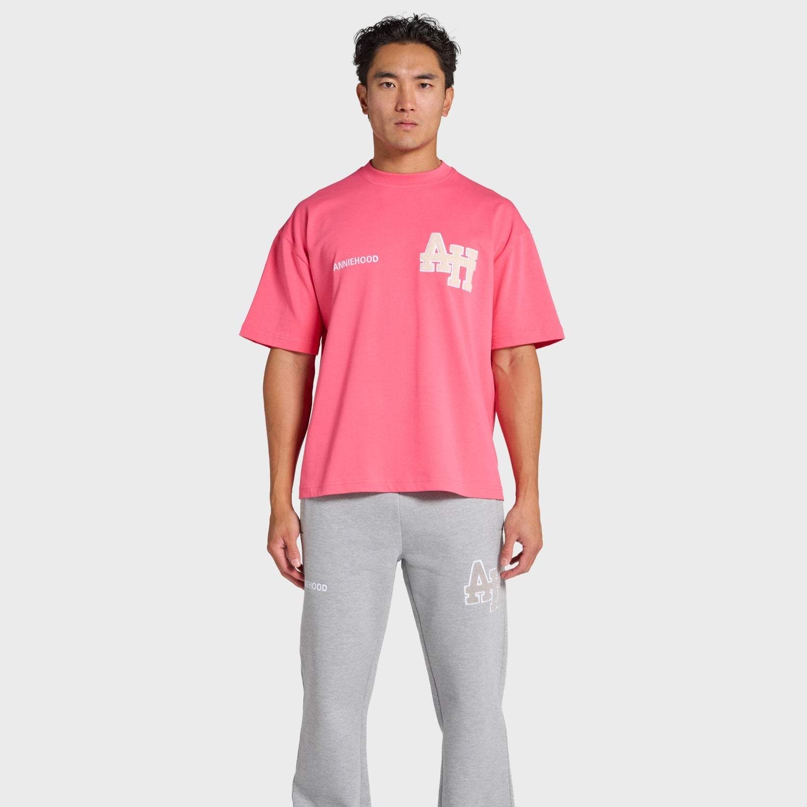 Man wearing pink ANNIE HOOD College T-shirt and gray sweatpants with logo