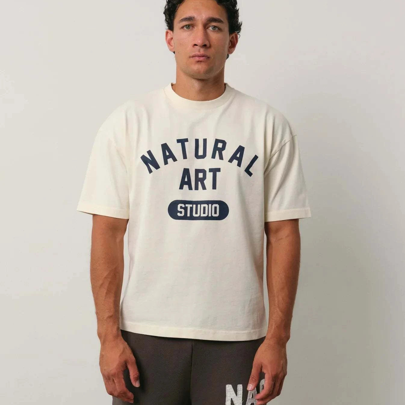 Natural Art Studio Varsity Tee with navy screen print on front, boxy fit, oversized drop shoulder, 100% cotton, worn by male model