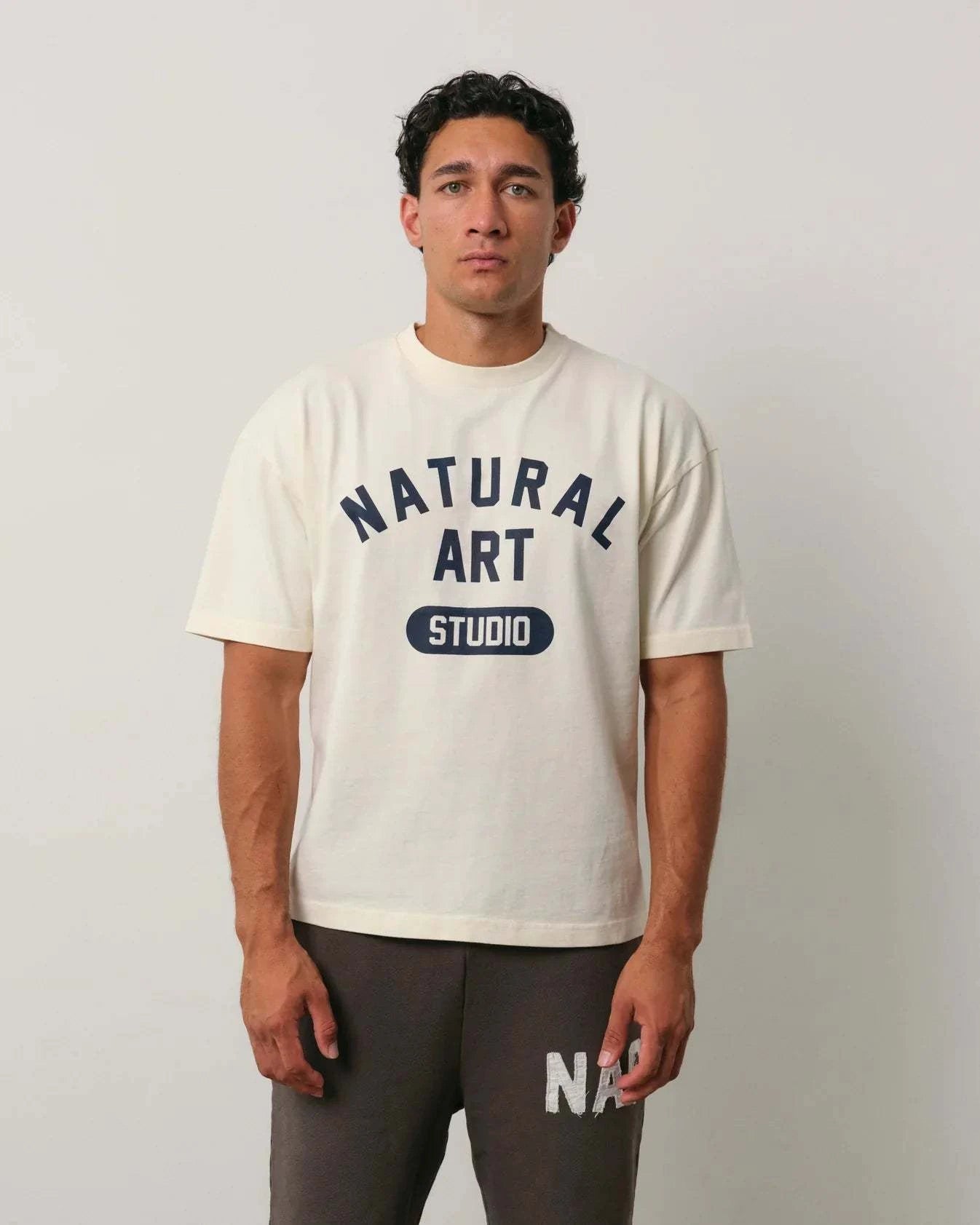 Natural Art Studio Varsity Tee with navy screen print on front, boxy fit, oversized drop shoulder, 100% cotton, worn by male model
