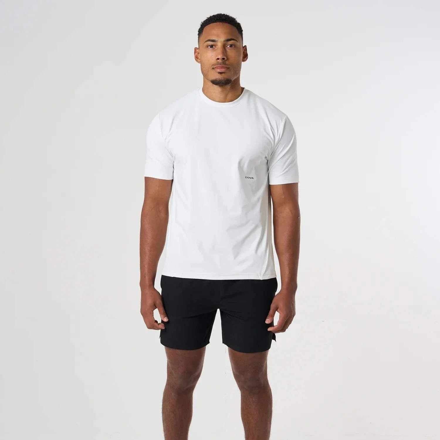 Man wearing white Cova Daily T-Shirt with black shorts standing against white background