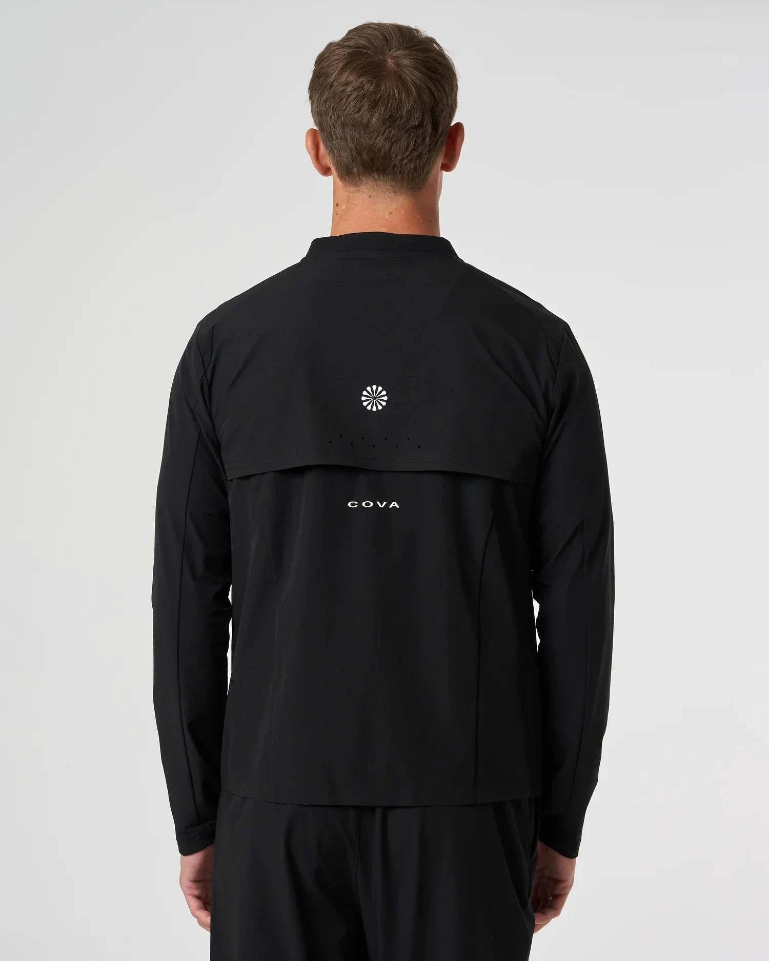 Back view of man wearing black Cova Daily Track Jacket with logo on upper back
