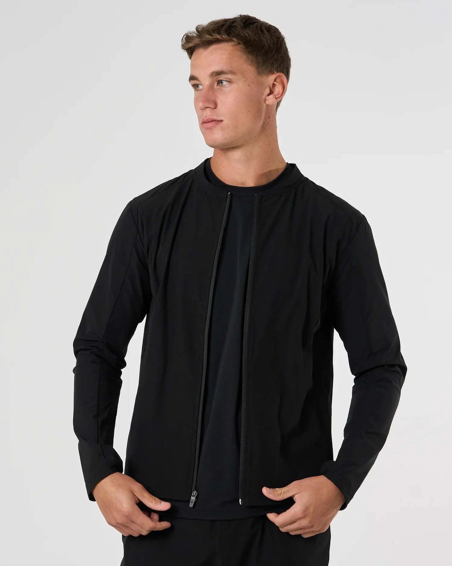 Man wearing black Cova Daily Track Jacket with front zipper and long sleeves against white background