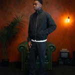 Man wearing Siarr Washed Quilted Bomber Jacket in Washed Black standing indoors with vintage decor background