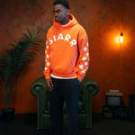 Man wearing orange Siarr Applique Hoodie with white stars on sleeves and kangaroo pocket