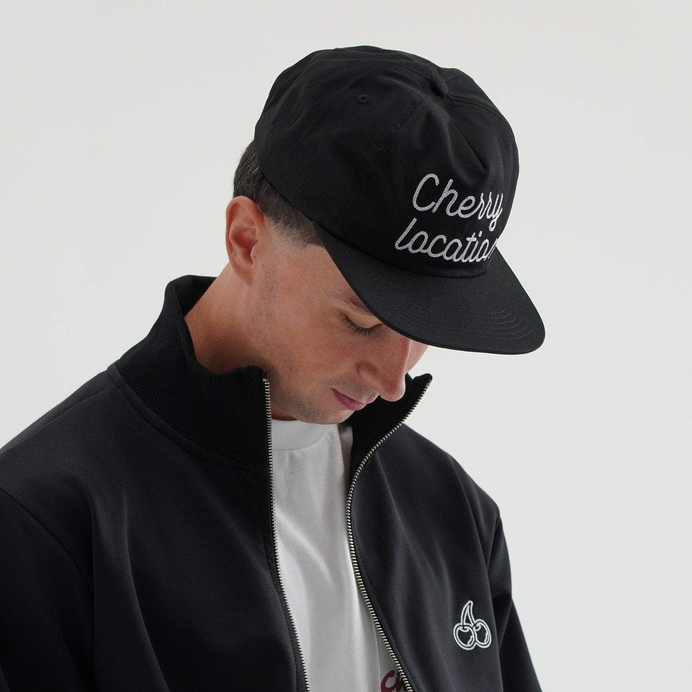 Man wearing Cherry Location black cap with embroidered text and black jacket with cherry logo
