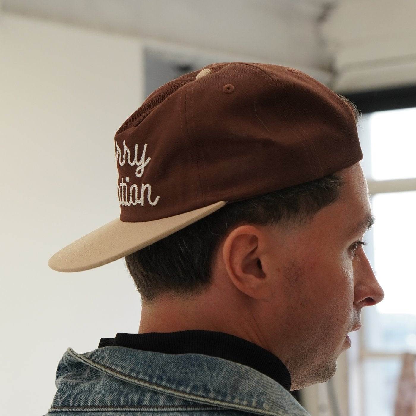 Cherry Location brown cap worn backward on man in denim jacket