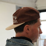 Cherry Location brown cap worn backward on man in denim jacket