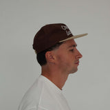 Cherry Location brown cap worn by man in white shirt side view
