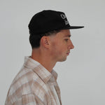 Side view of man wearing Cherry Location Black Cap with embroidered text
