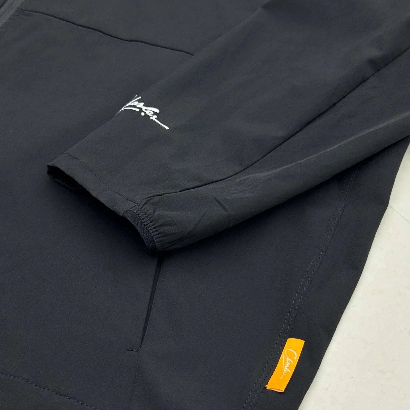 Close-up of Studio By Charles black track jacket sleeve and pocket with logo tags